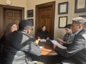 Four YALL students sit around a wooden circular table while speaking to a staffer from Rep. Torres' office.